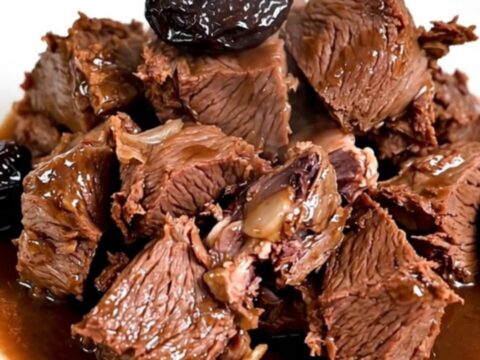 A bowl of slow-cooked beef chunks with glossy red wine sauce and plump prunes.