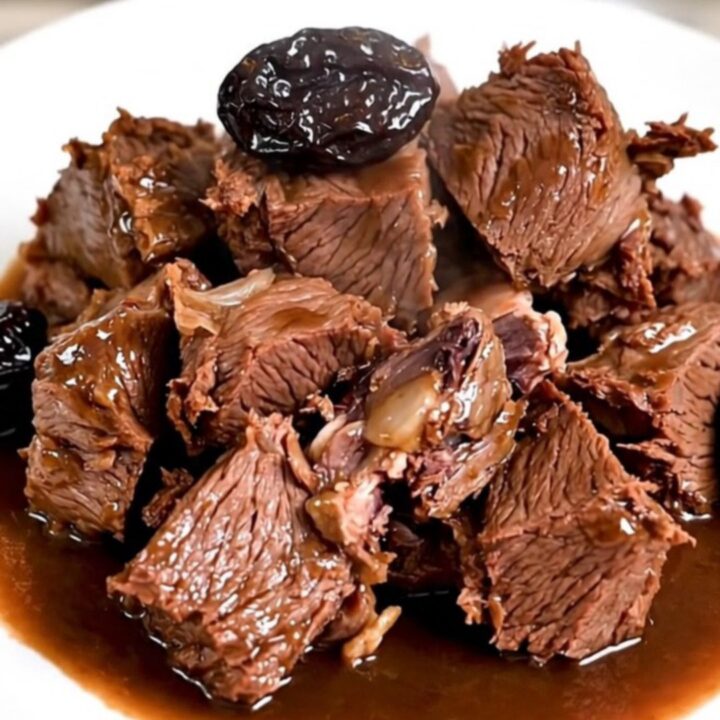 A bowl of slow-cooked beef chunks with glossy red wine sauce and plump prunes.