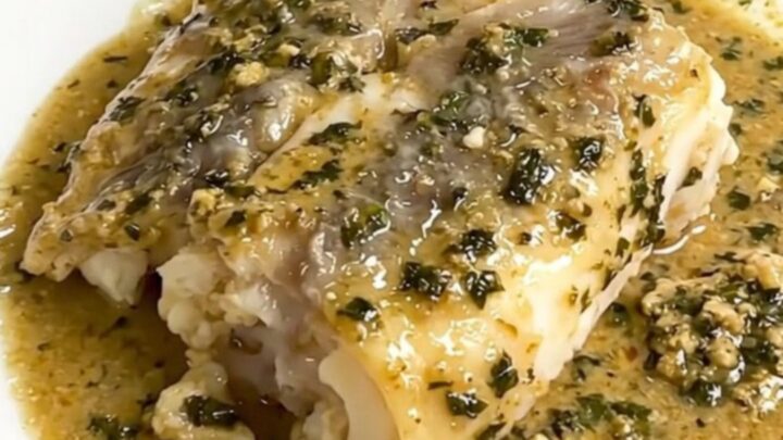 A close-up of tender monkfish pieces covered in a creamy tarragon sauce served on a white plate.