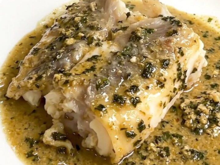 A close-up of tender monkfish pieces covered in a creamy tarragon sauce served on a white plate.