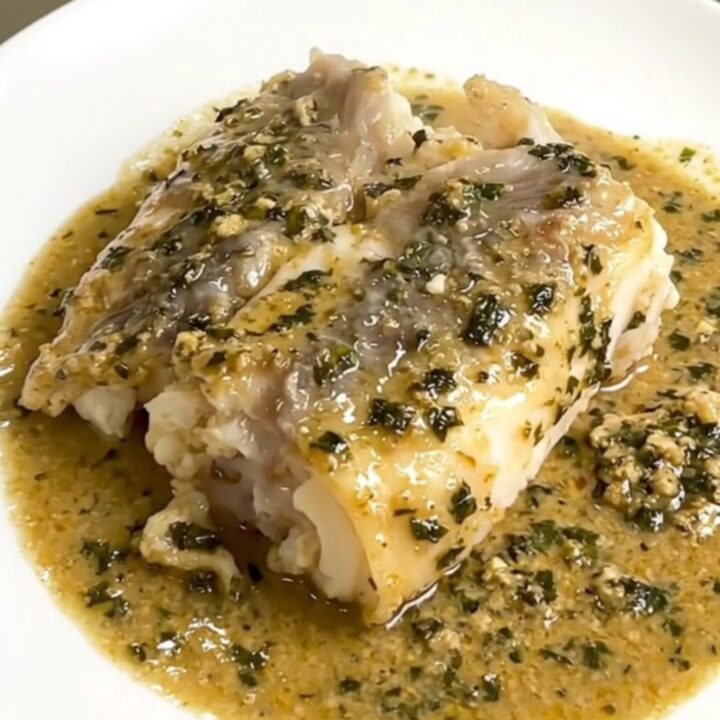 A close-up of tender monkfish pieces covered in a creamy tarragon sauce served on a white plate.