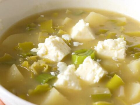 A white bowl filled with creamy, steaming leek and potato soup garnished with melted Cantal cheese.