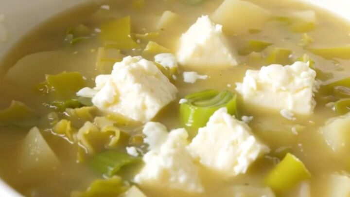 A white bowl filled with creamy, steaming leek and potato soup garnished with melted Cantal cheese.