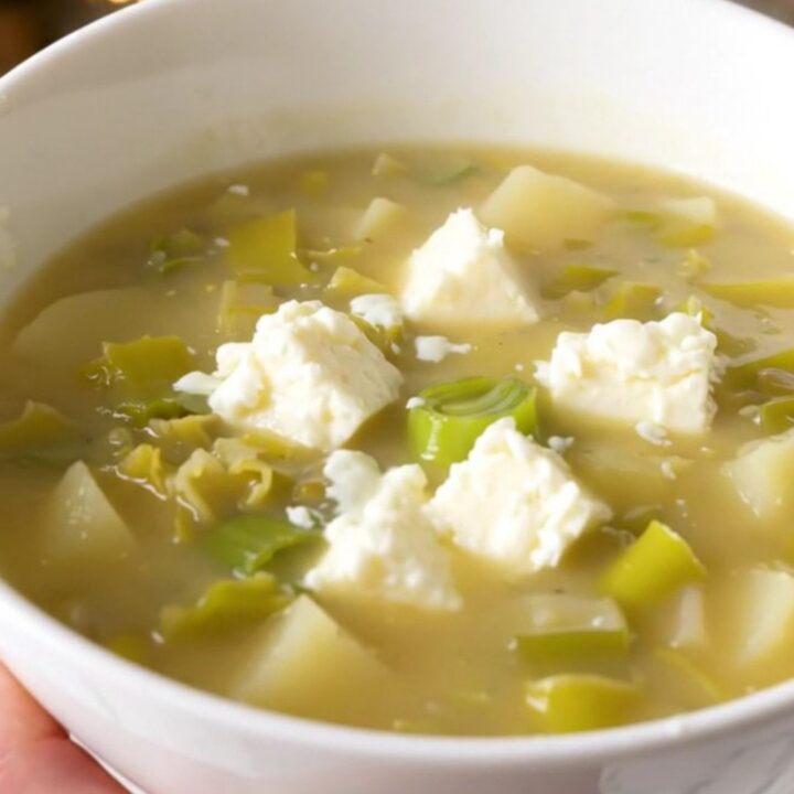 A white bowl filled with creamy, steaming leek and potato soup garnished with melted Cantal cheese.