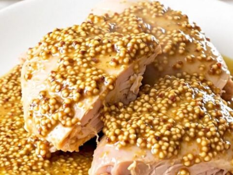 A close-up of a succulent turkey thigh covered in a creamy leek and mustard sauce on a white plate.