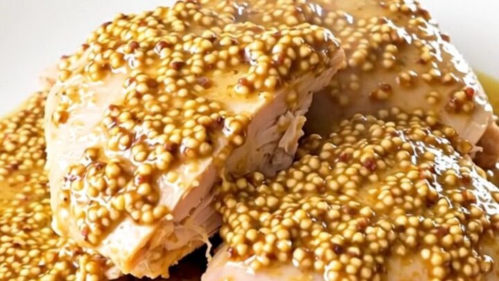A close-up of a succulent turkey thigh covered in a creamy leek and mustard sauce on a white plate.