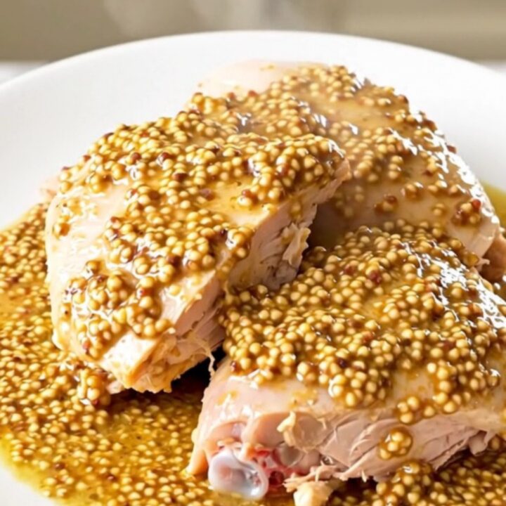 A close-up of a succulent turkey thigh covered in a creamy leek and mustard sauce on a white plate.