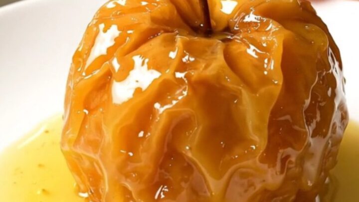 Four stuffed apples arranged in a slow cooker, topped with nuts and butter.