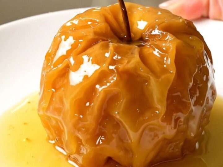 Four stuffed apples arranged in a slow cooker, topped with nuts and butter.