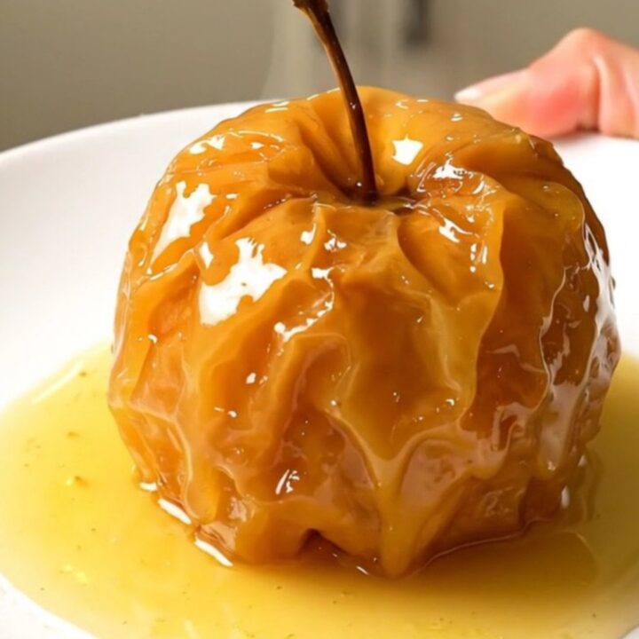 Four stuffed apples arranged in a slow cooker, topped with nuts and butter.
