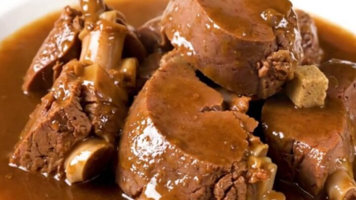 A rustic slow cooker filled with tender veal stew, potatoes, and onions in a rich, glossy broth.