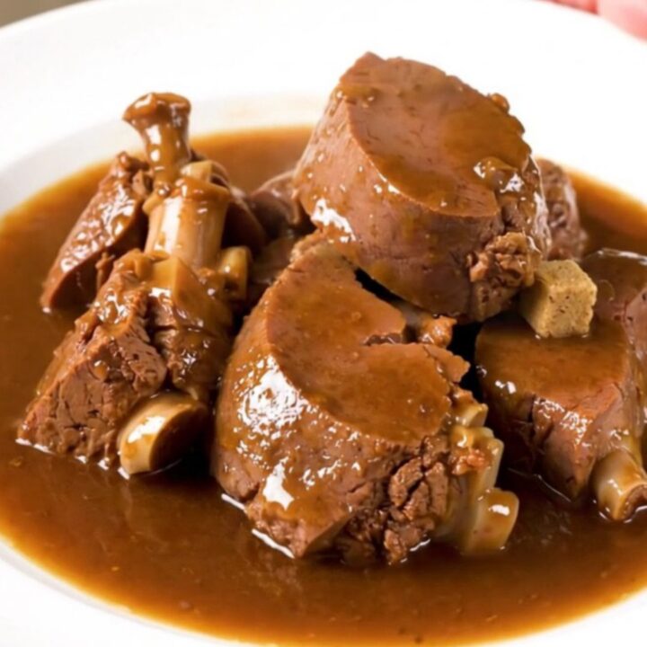 A rustic slow cooker filled with tender veal stew, potatoes, and onions in a rich, glossy broth.