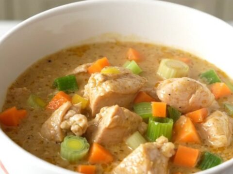 A close-up of a creamy chicken waterzooi in a white ceramic bowl, showing tender chicken and vegetables in a rich sauce.