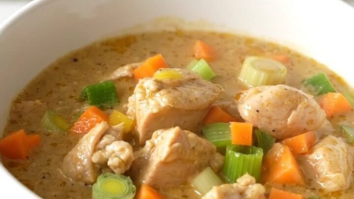 A close-up of a creamy chicken waterzooi in a white ceramic bowl, showing tender chicken and vegetables in a rich sauce.