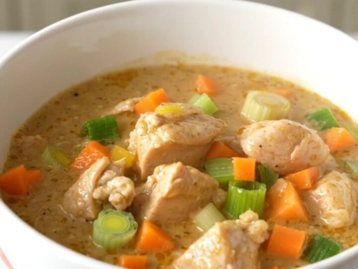 A close-up of a creamy chicken waterzooi in a white ceramic bowl, showing tender chicken and vegetables in a rich sauce.