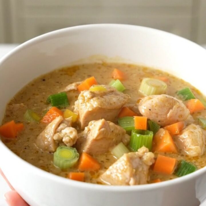 A close-up of a creamy chicken waterzooi in a white ceramic bowl, showing tender chicken and vegetables in a rich sauce.
