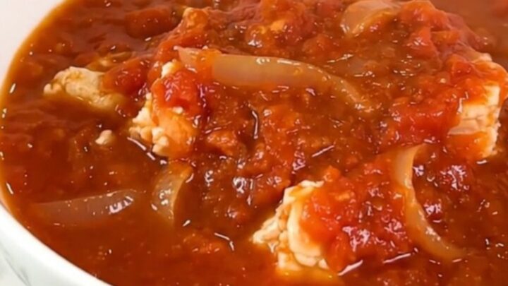 A vibrant Creole salt cod rougail in a black slow cooker, showcasing pieces of fish in a rich tomato sauce.