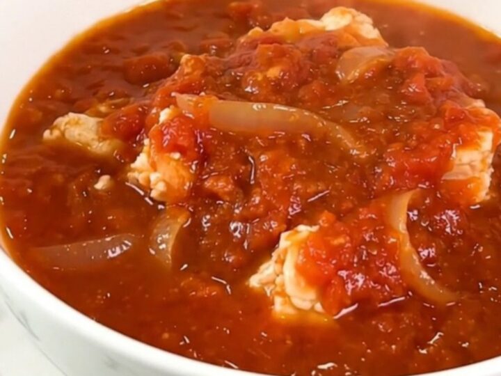 A vibrant Creole salt cod rougail in a black slow cooker, showcasing pieces of fish in a rich tomato sauce.