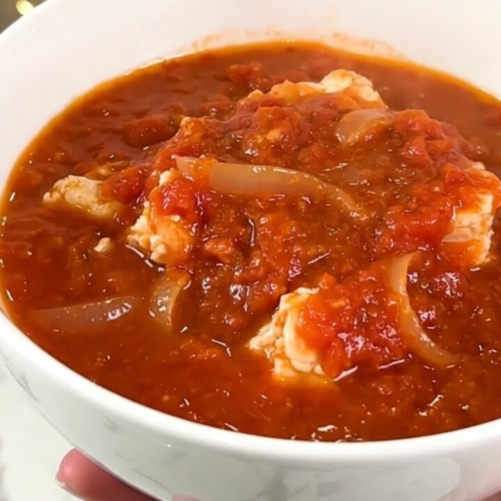 A vibrant Creole salt cod rougail in a black slow cooker, showcasing pieces of fish in a rich tomato sauce.