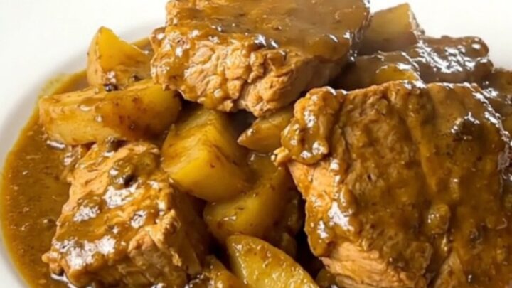 A white plate holding tender chunks of pork coated in a creamy golden curry sauce with soft, glazed apple slices.