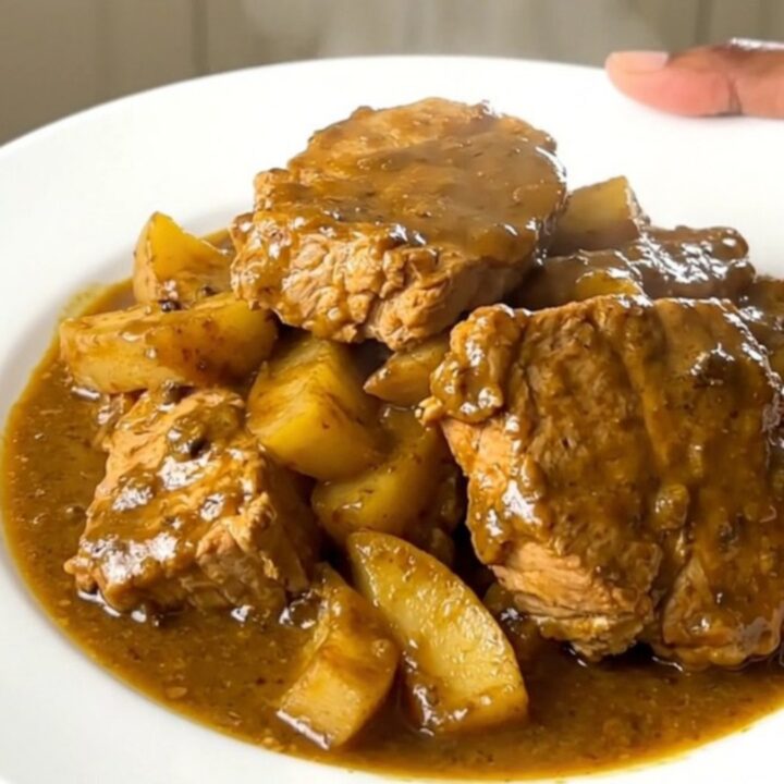 A white plate holding tender chunks of pork coated in a creamy golden curry sauce with soft, glazed apple slices.