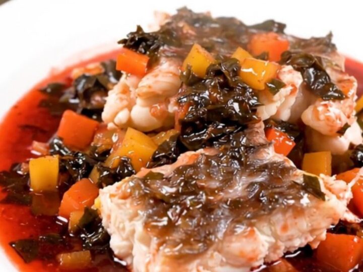 A top-down view of a slow cooker filled with white fish, mushrooms, and pearl onions in a rich red wine sauce.