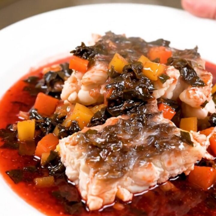 A top-down view of a slow cooker filled with white fish, mushrooms, and pearl onions in a rich red wine sauce.