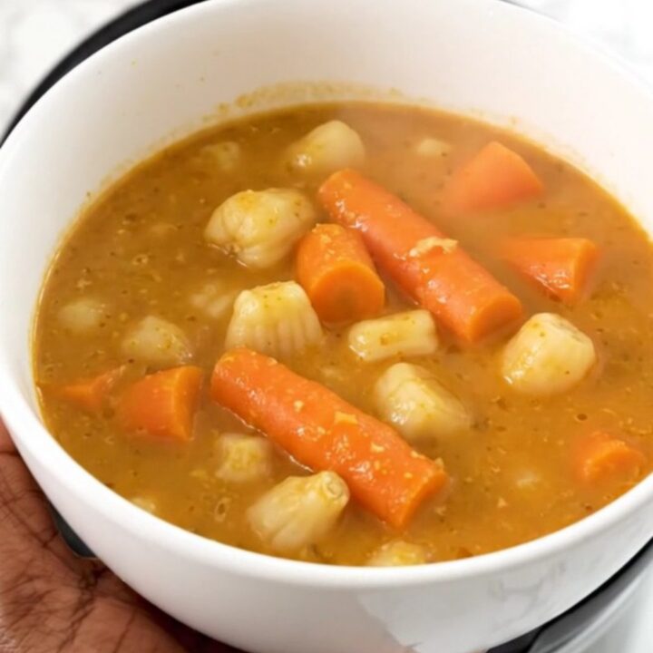 A white bowl filled with creamy slow-cooked sunchoke and carrot stew, garnished with fresh tarragon.