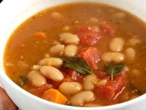 A steaming white bowl filled with white bean, tomato, and sage soup