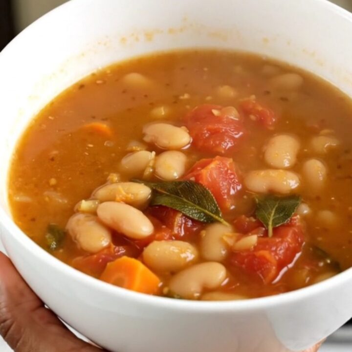 A steaming white bowl filled with white bean, tomato, and sage soup