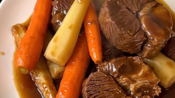 Close-up of tender glazed beef cheeks served with carrots and parsnips on a white plate.