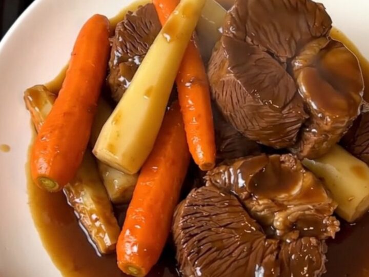 Close-up of tender glazed beef cheeks served with carrots and parsnips on a white plate.