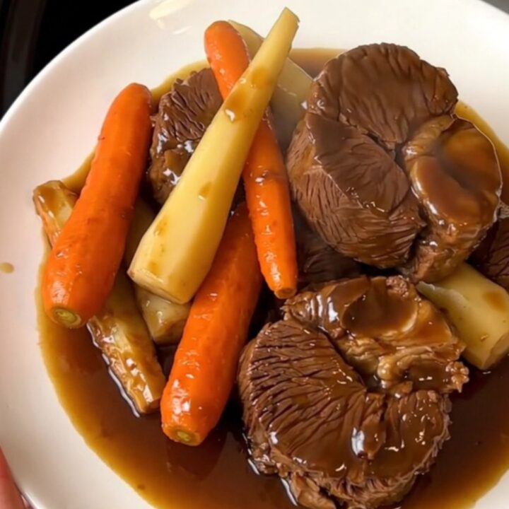 Close-up of tender glazed beef cheeks served with carrots and parsnips on a white plate.