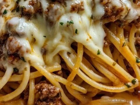 A close-up of a fork lifting a large portion of spaghetti coated in a rich, golden cheese and beef sauce.