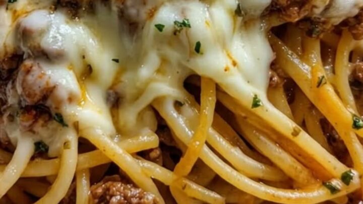 A close-up of a fork lifting a large portion of spaghetti coated in a rich, golden cheese and beef sauce.