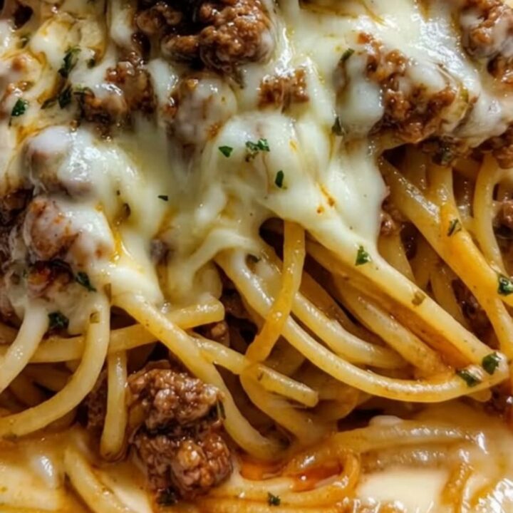 A close-up of a fork lifting a large portion of spaghetti coated in a rich, golden cheese and beef sauce.