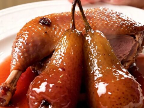 A glossy, slow-cooked duck leg served with a tender poached pear on a white plate.