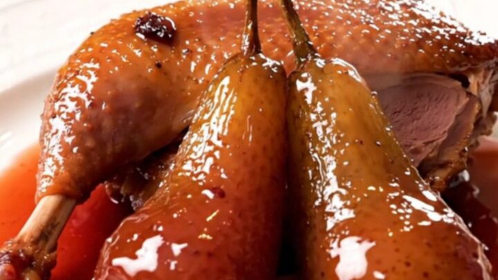 A glossy, slow-cooked duck leg served with a tender poached pear on a white plate.
