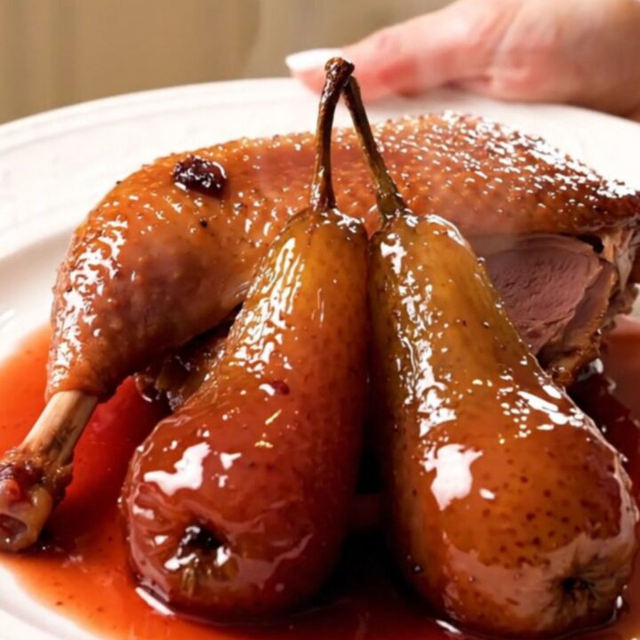 A glossy, slow-cooked duck leg served with a tender poached pear on a white plate.