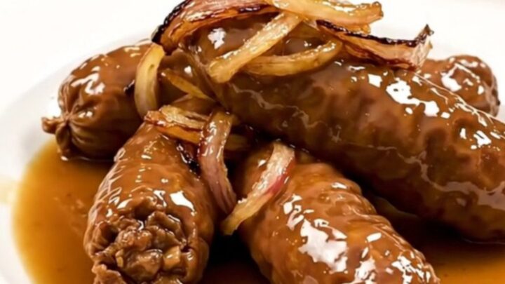 Four golden-brown andouillettes cooked in a white wine and shallot reduction in a slow cooker.