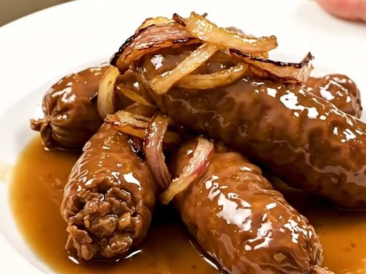 Four golden-brown andouillettes cooked in a white wine and shallot reduction in a slow cooker.