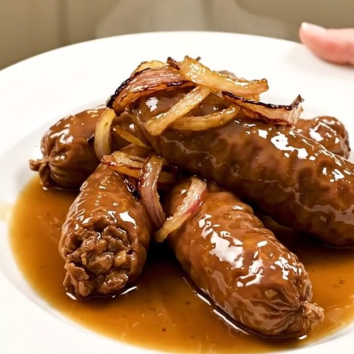 Four golden-brown andouillettes cooked in a white wine and shallot reduction in a slow cooker.