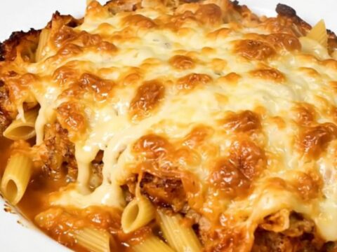 A top-down view of a steaming tuna and emmental pasta bake in a black slow cooker on a speckled countertop.