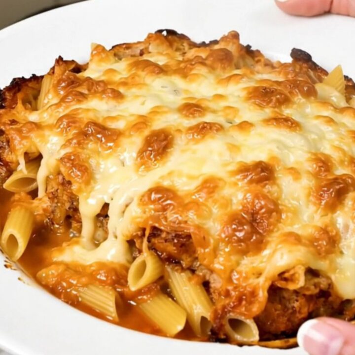A top-down view of a steaming tuna and emmental pasta bake in a black slow cooker on a speckled countertop.