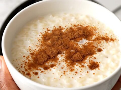 A top-down view of a black slow cooker filled with rice, milk, and spices on a white speckled countertop.