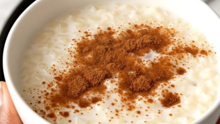 A top-down view of a black slow cooker filled with rice, milk, and spices on a white speckled countertop.
