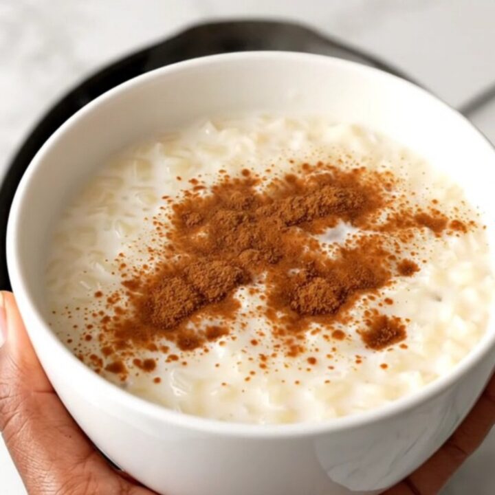 A top-down view of a black slow cooker filled with rice, milk, and spices on a white speckled countertop.