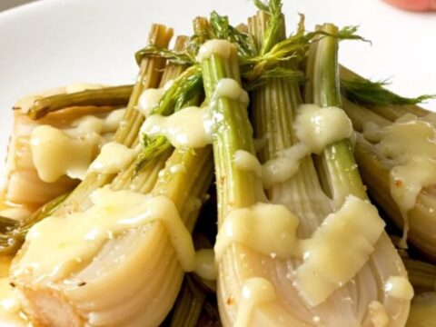 A top-down view of tender, braised fennel wedges in a slow cooker, topped with melted golden Parmesan cheese.