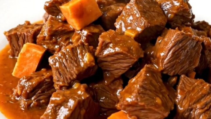 A top-down view of a black oval slow cooker filled with chunks of beef, diced sweet potatoes, and broth.