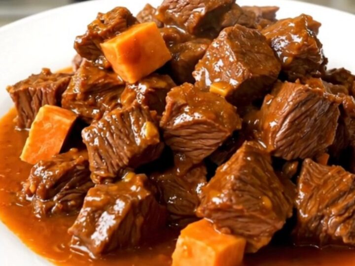 A top-down view of a black oval slow cooker filled with chunks of beef, diced sweet potatoes, and broth.